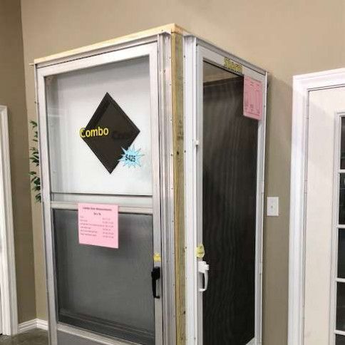 A silver screen door with a glass panel and a black diamond logo labeled