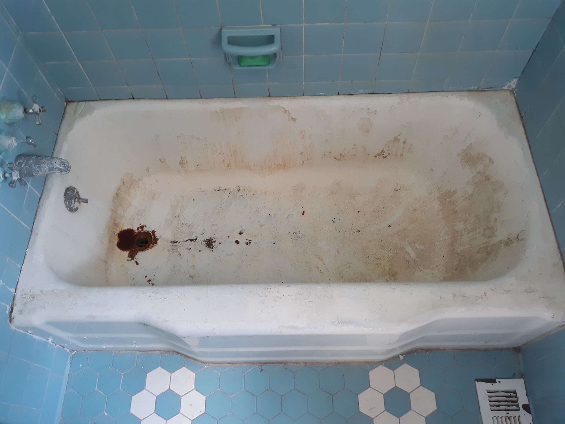 A dirty bathtub in a bathroom with blue tiles.