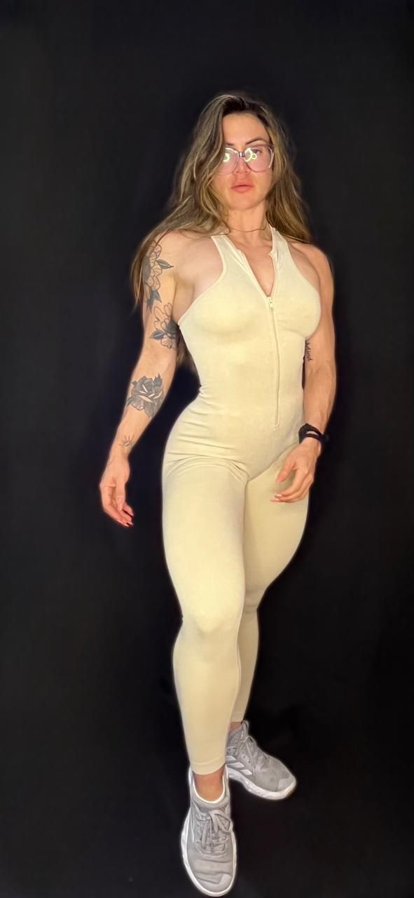 Una mujer con un mono amarillo está parada frente a un fondo negro.