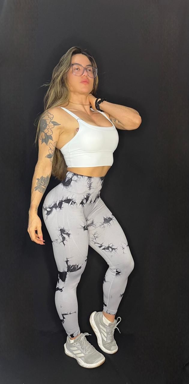 Una mujer con una camiseta blanca sin mangas y leggings teñidos está parada frente a un fondo negro.