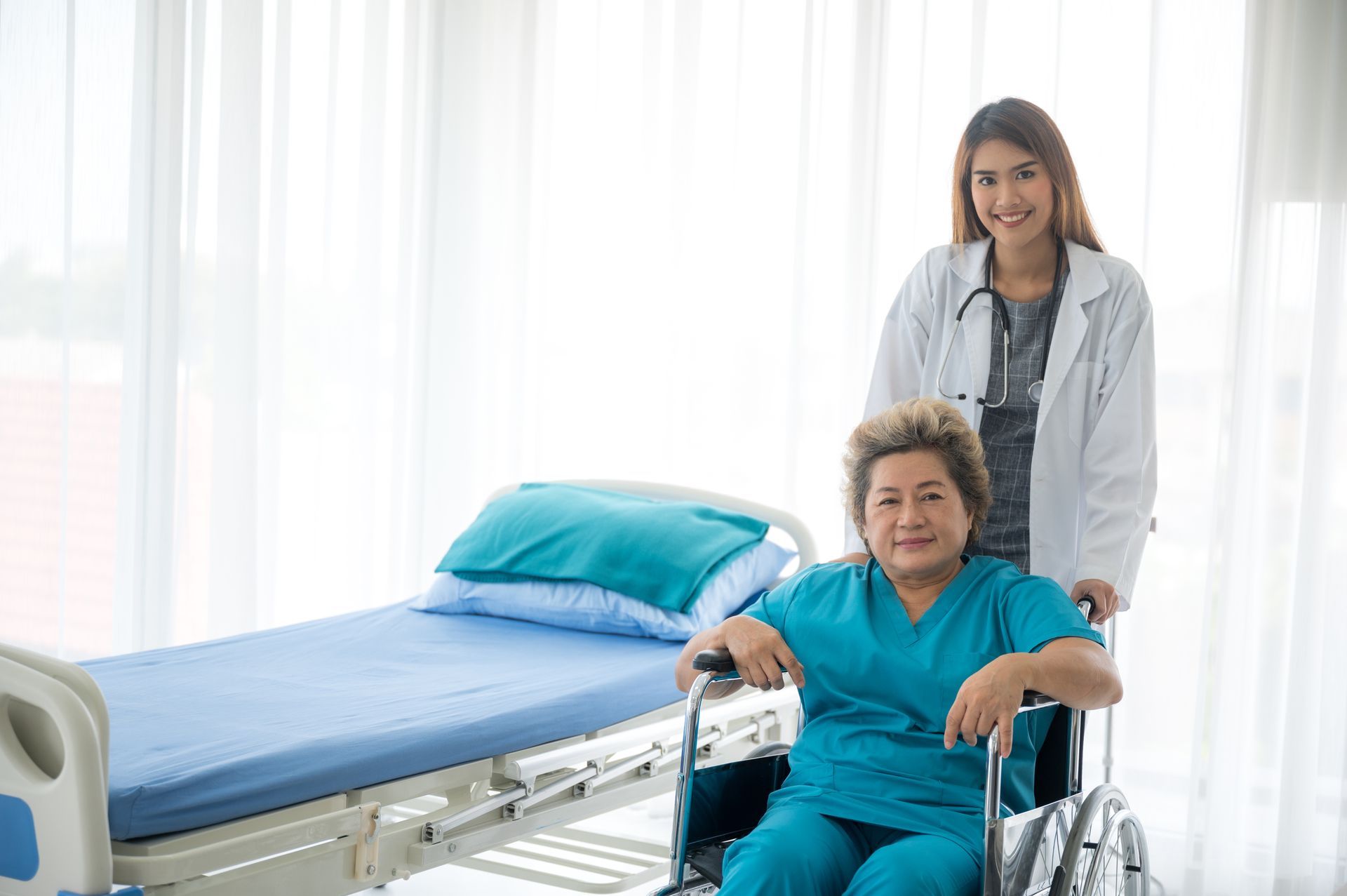 Doctor pushing a person in a wheelchair in a hospital room with a bed; both smiling.