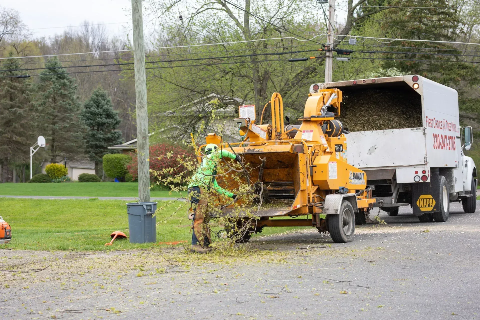 Tree branches being fed into a wood chipper truck in a suburban neighborhood.