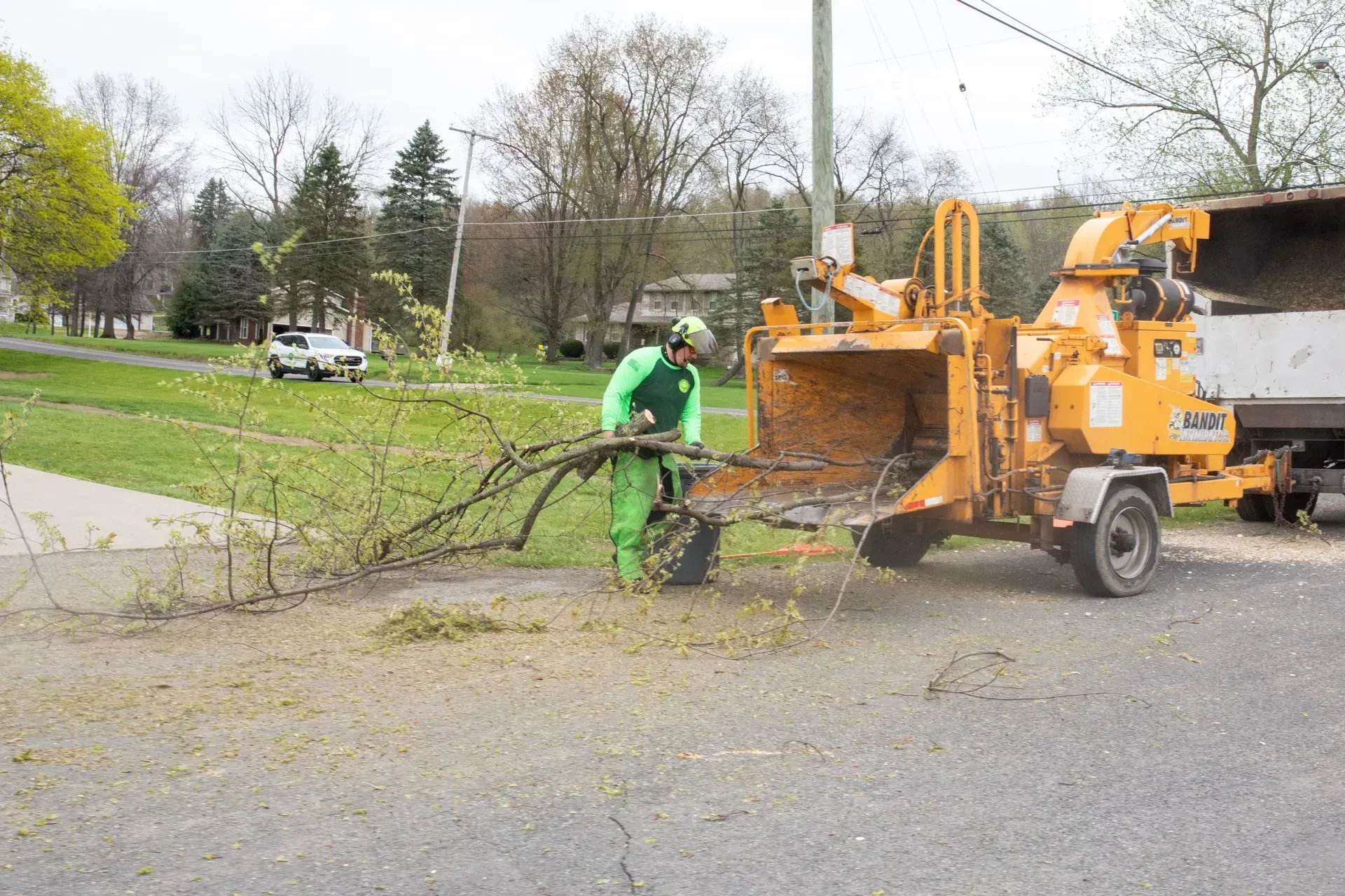 Man in green safety gear feeding tree branches into a wood chipper on a street.