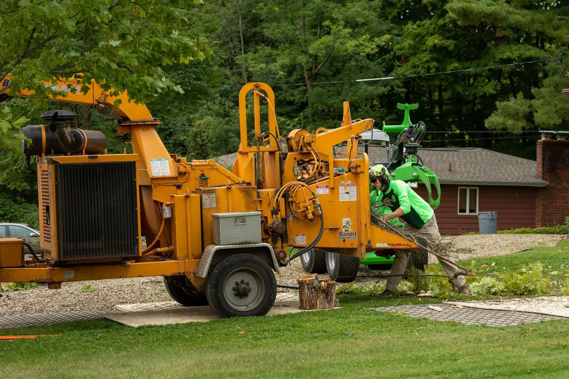 A wood chipper being operated by a person wearing a green shirt outdoors near a building.