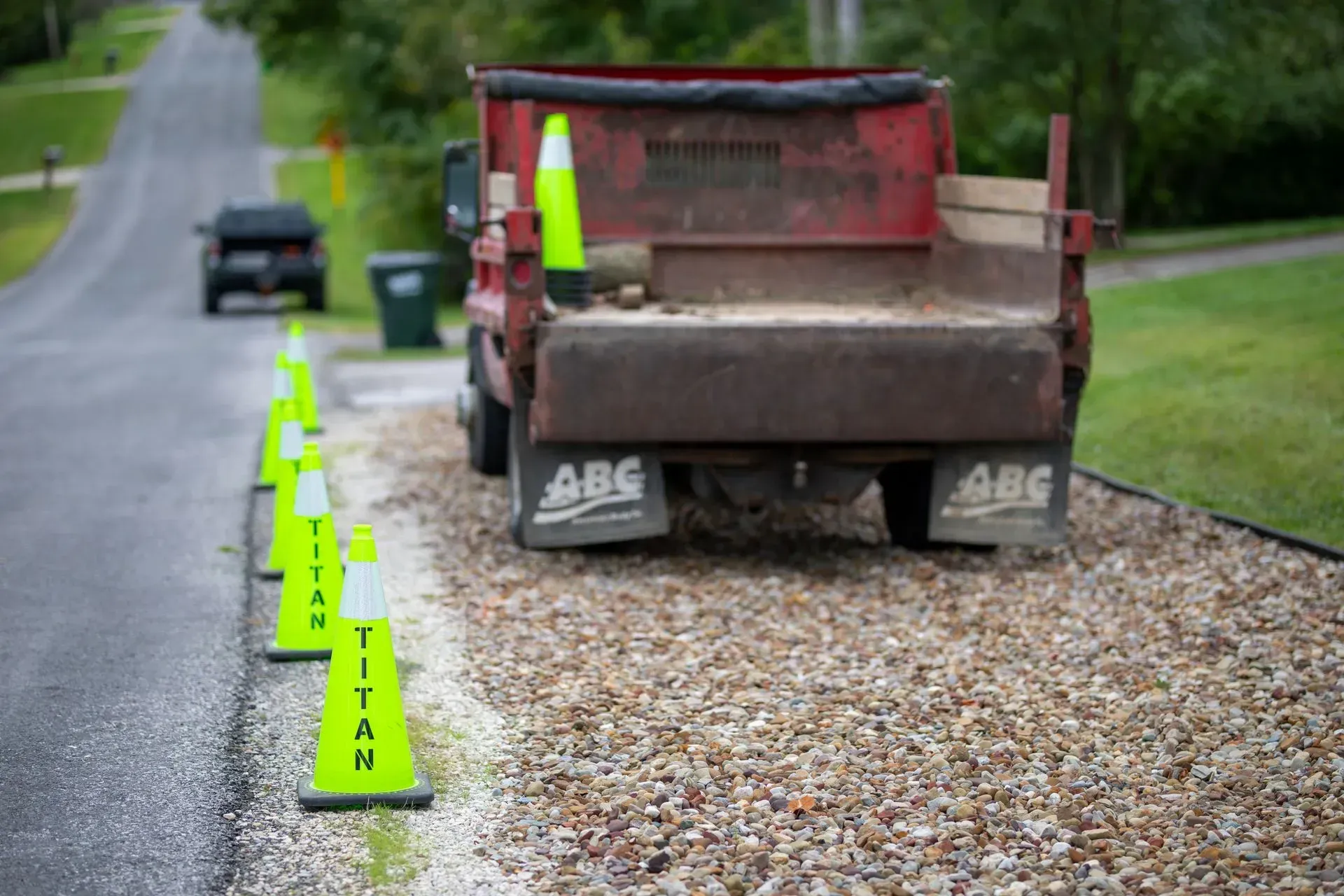 A gravel driveway with a red dump truck and traffic cones on the edge of the road.