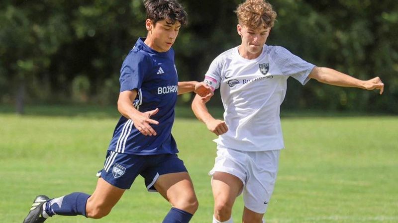 Sporting Arkansas boys players controlling ball near opposing player.