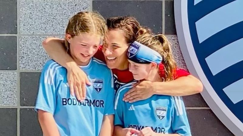 Soccer parent hugging two young girl soccer players.
