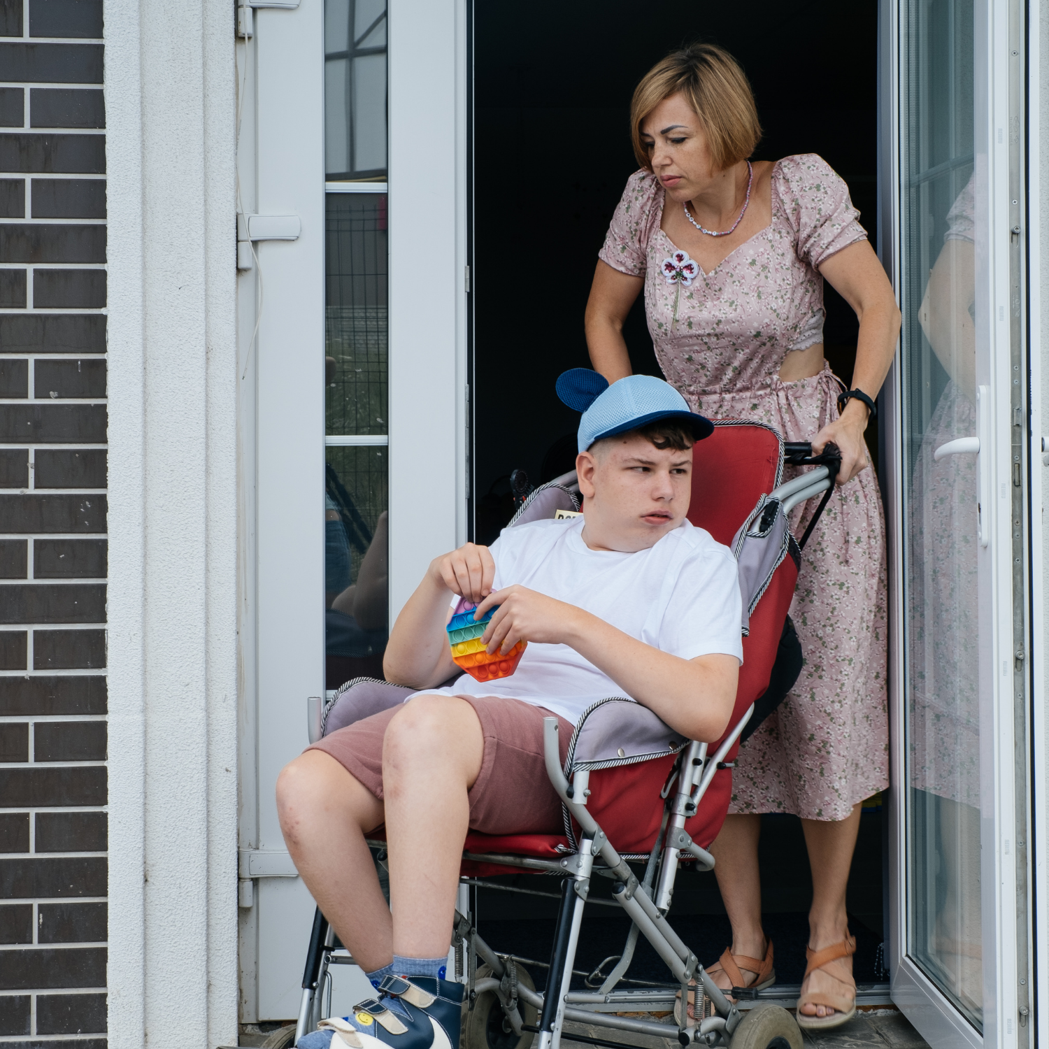 Woman pushing out a young man with disability in a wheelchair outside of the house