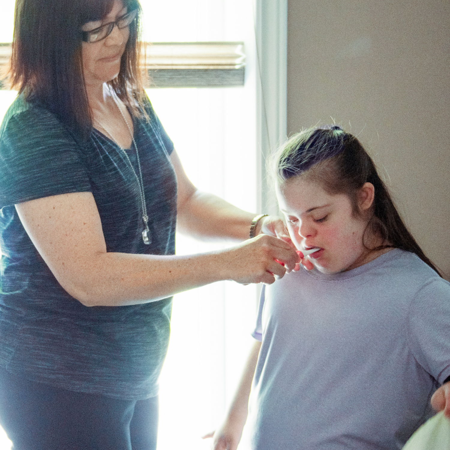 a woman is helping a girl with down syndrome put on a shirt