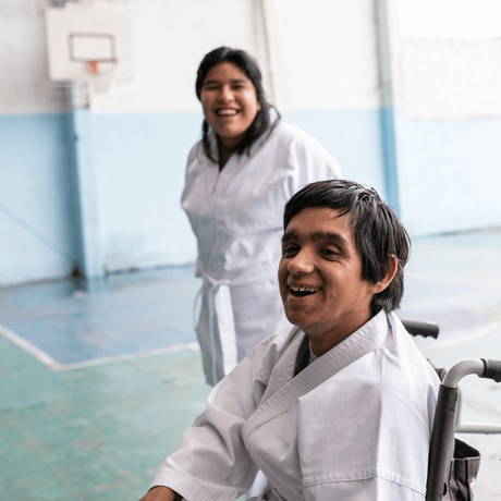 Man with disability sitting on a wheelchair while wearing a martial arts uniform, woman standing behind him