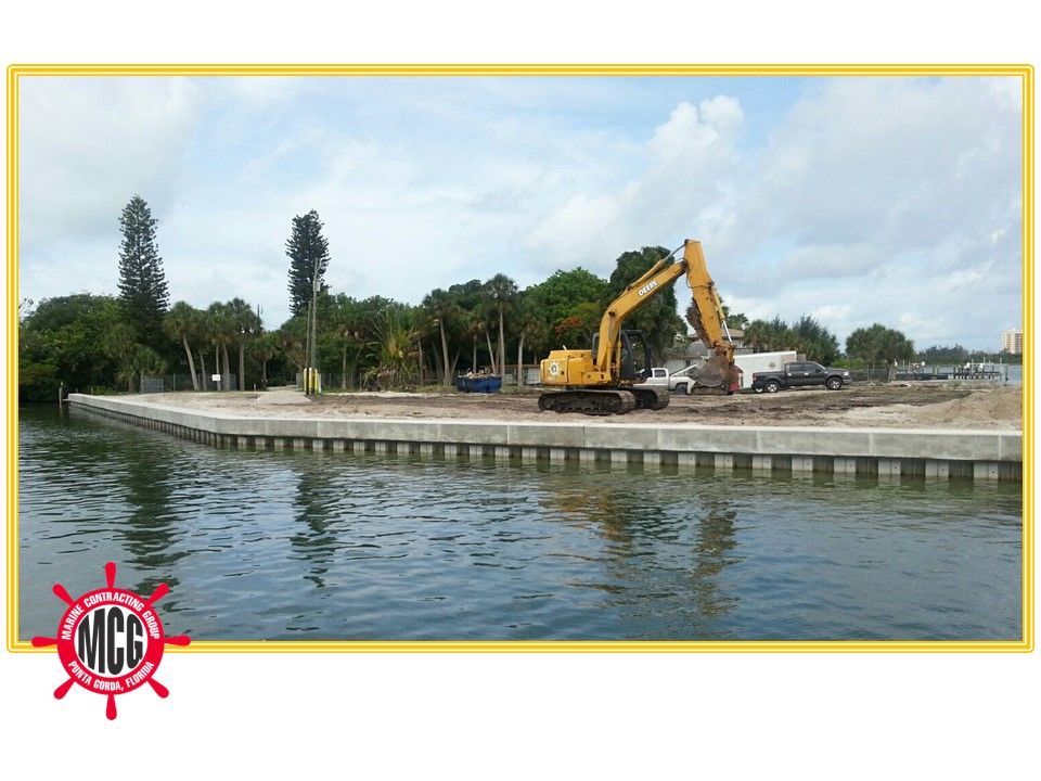 A large yellow excavator is working on a dock in the water - Punta Gorda, FL - Marine Contracting Group Inc