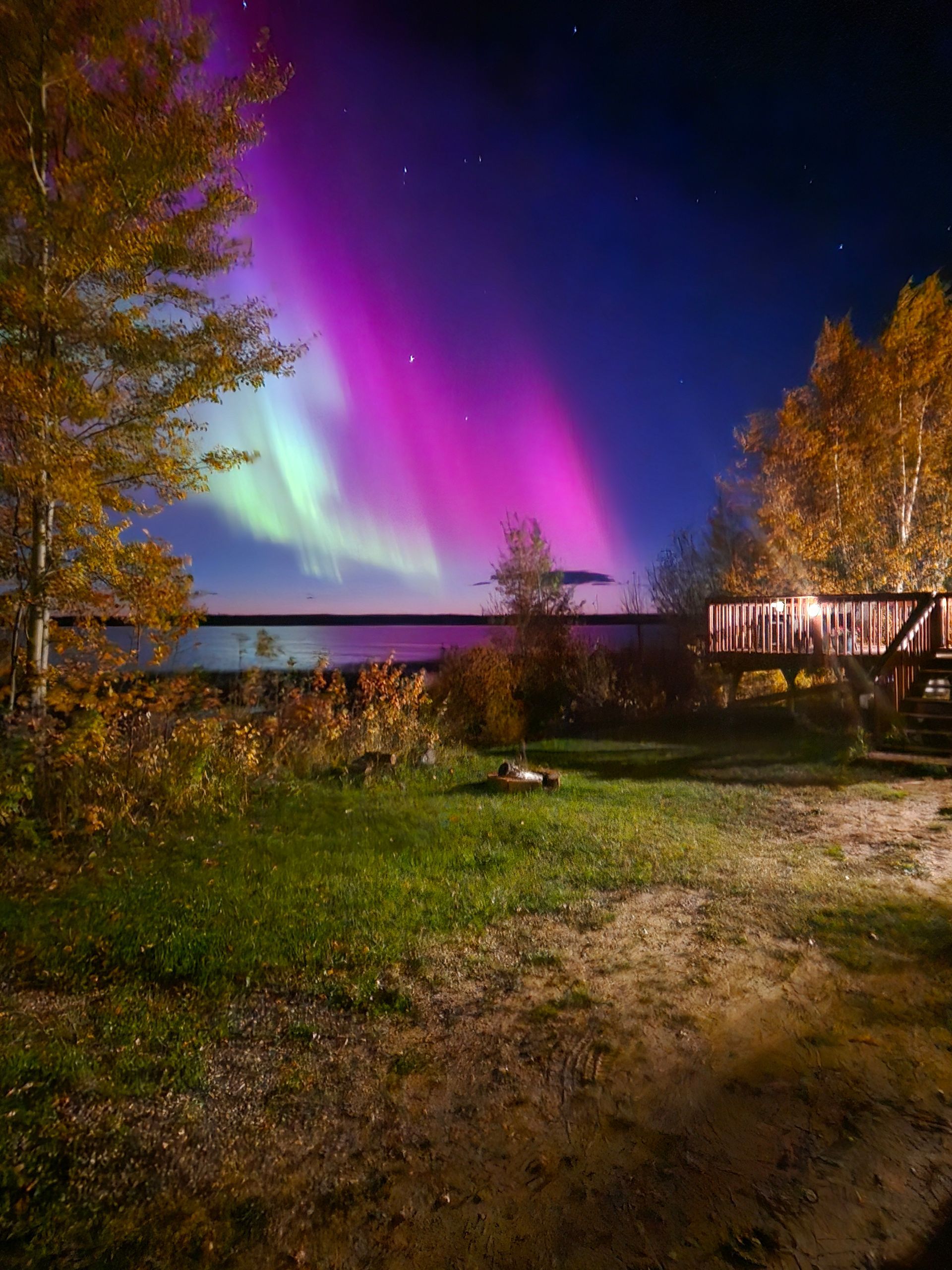 Aurora borealis in shades of pink, green, and blue over a lake, with a cabin on the shore.