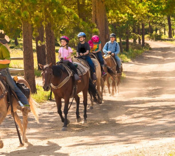 Group of children horseback riding on a dirt path in a forest.