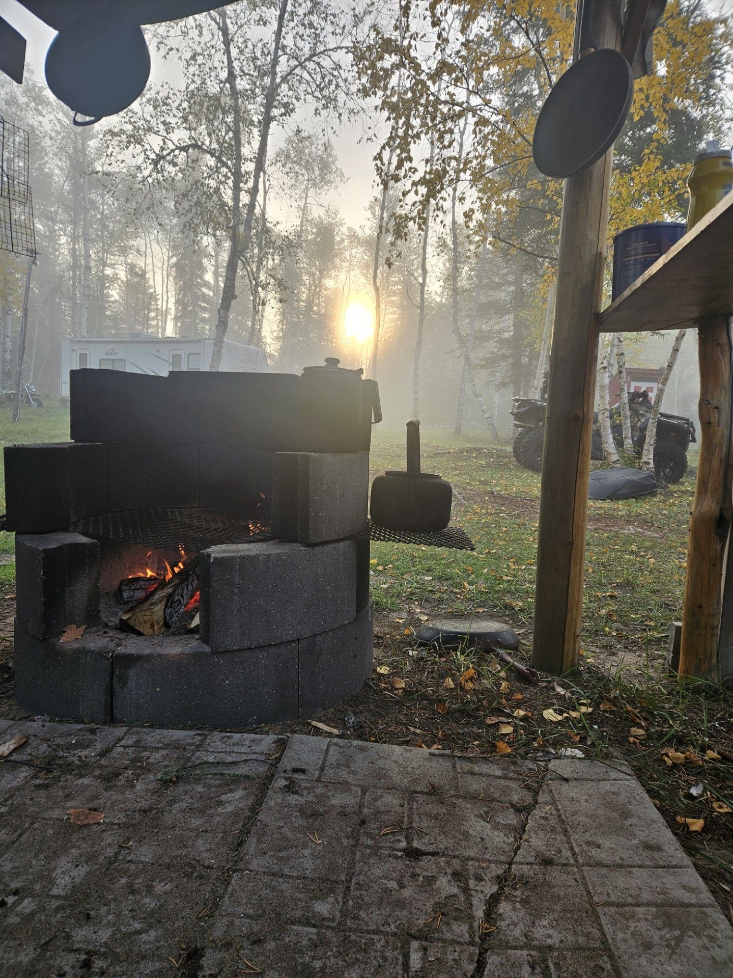 Fire pit made of stacked blocks with a fire burning outdoors, foggy background.