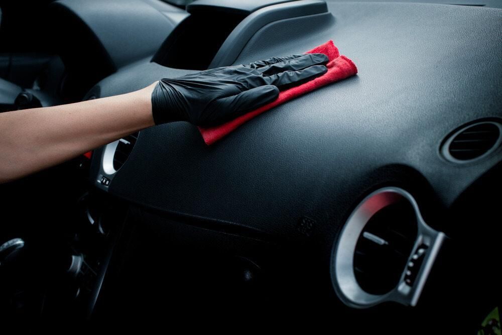 A Person Wearing Black Gloves is Cleaning the Dashboard of a Car With a Red Cloth — Precise Detailing Specialists in Emerald, QLD