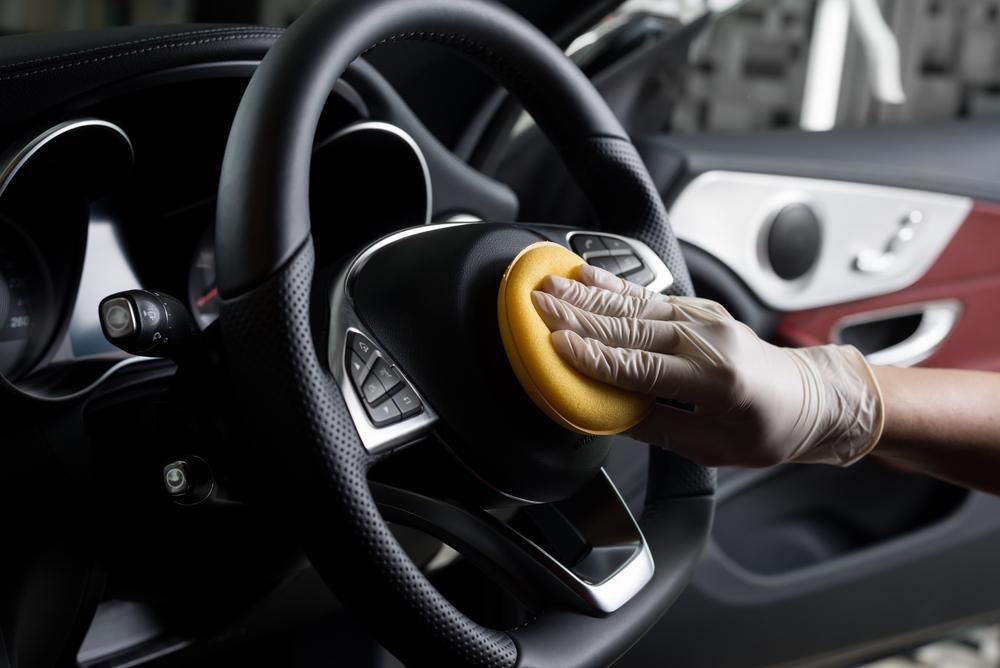 A Person is Cleaning the Steering Wheel of a Car With a Sponge — Precise Detailing Specialists in Emerald, QLD