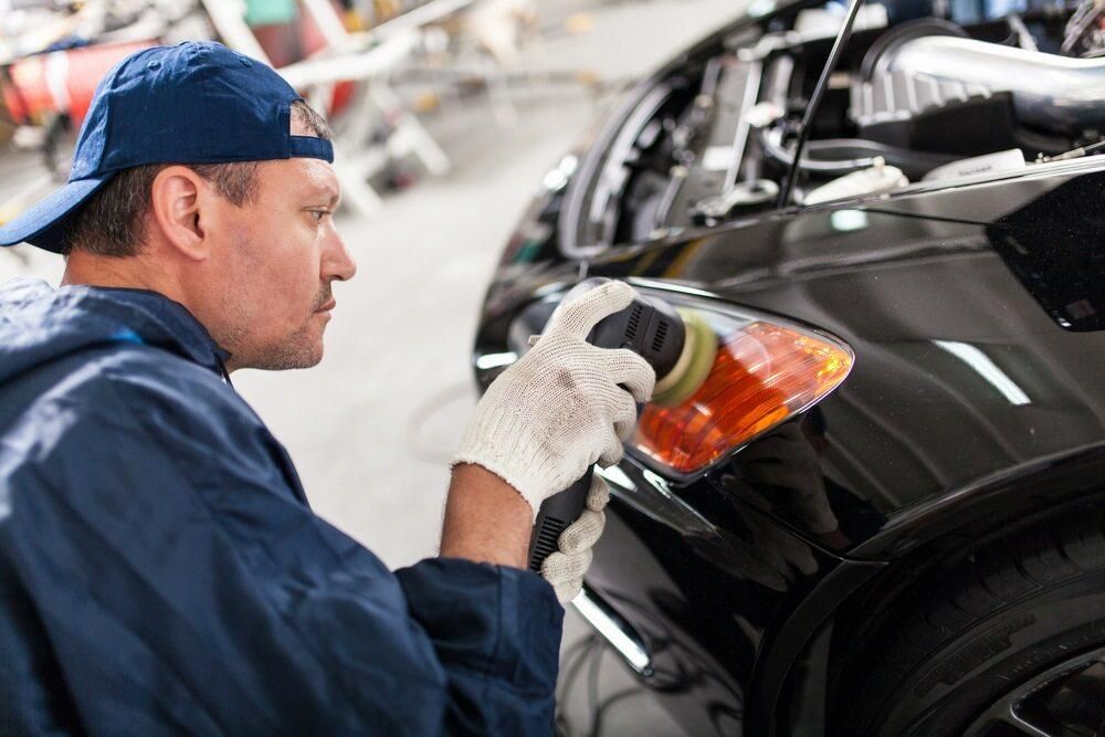 A Man is Polishing the Headlight of a Car in a Garage — Precise Detailing Specialists in Emerald QLD