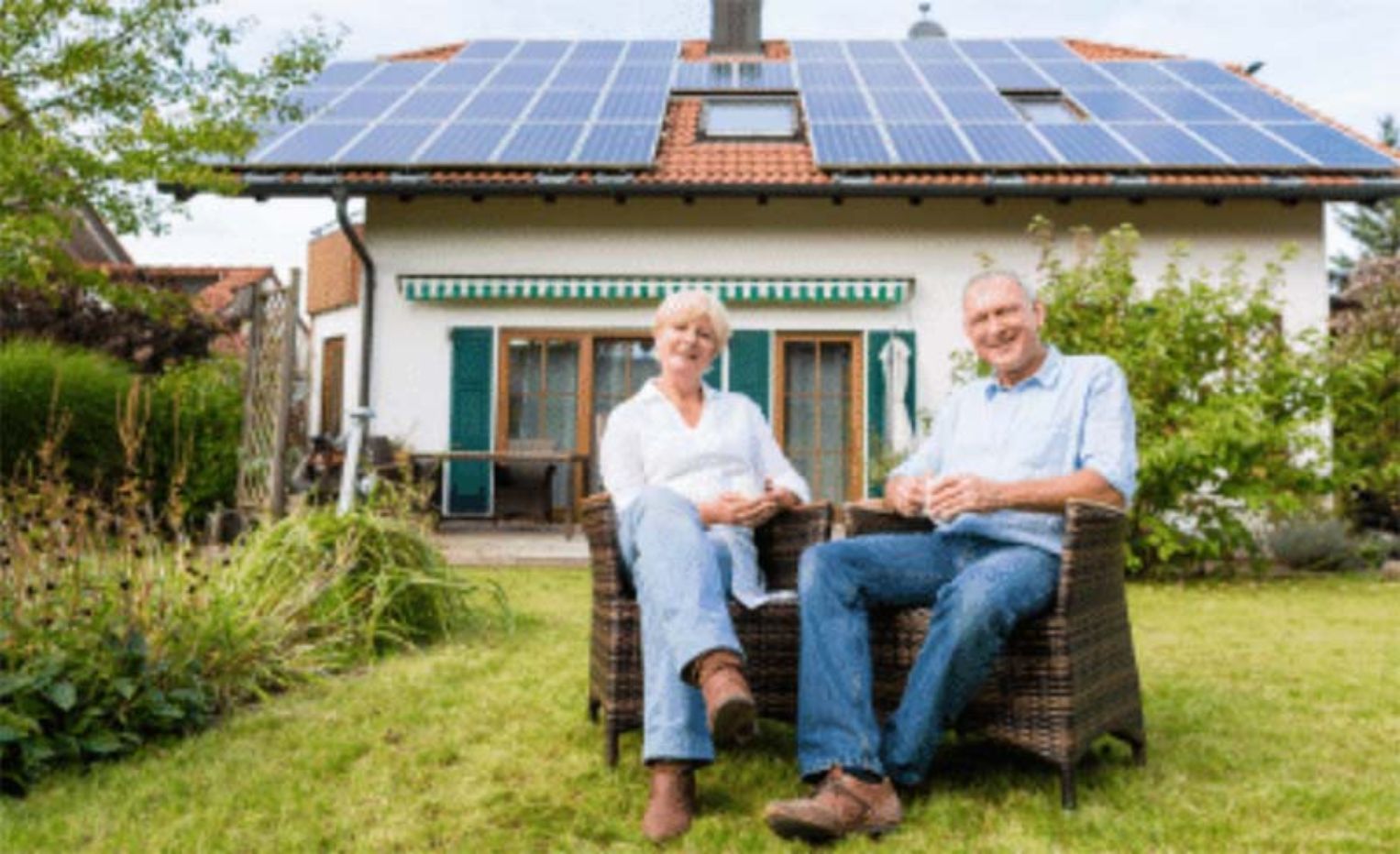A man and a woman are sitting in chairs in front of a house with solar panels on the roof.