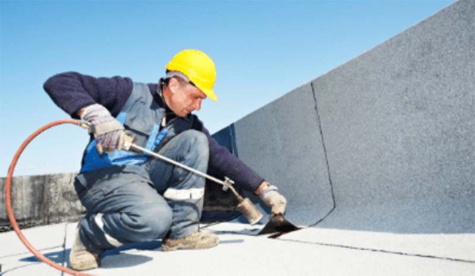 A man is kneeling down on the ground using a torch on a roof.