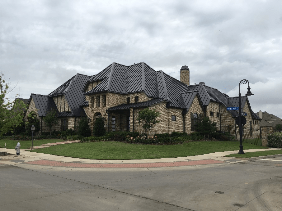 A large house with a black roof is sitting on the corner of a street.