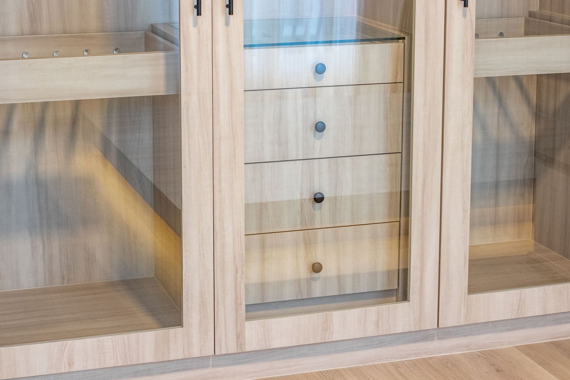 A close up of a wooden wardrobe with glass doors and drawers.