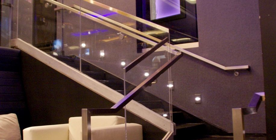A staircase with a glass railing and a chair in the background.