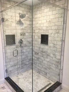 A shower stall with a glass door and marble tiles.