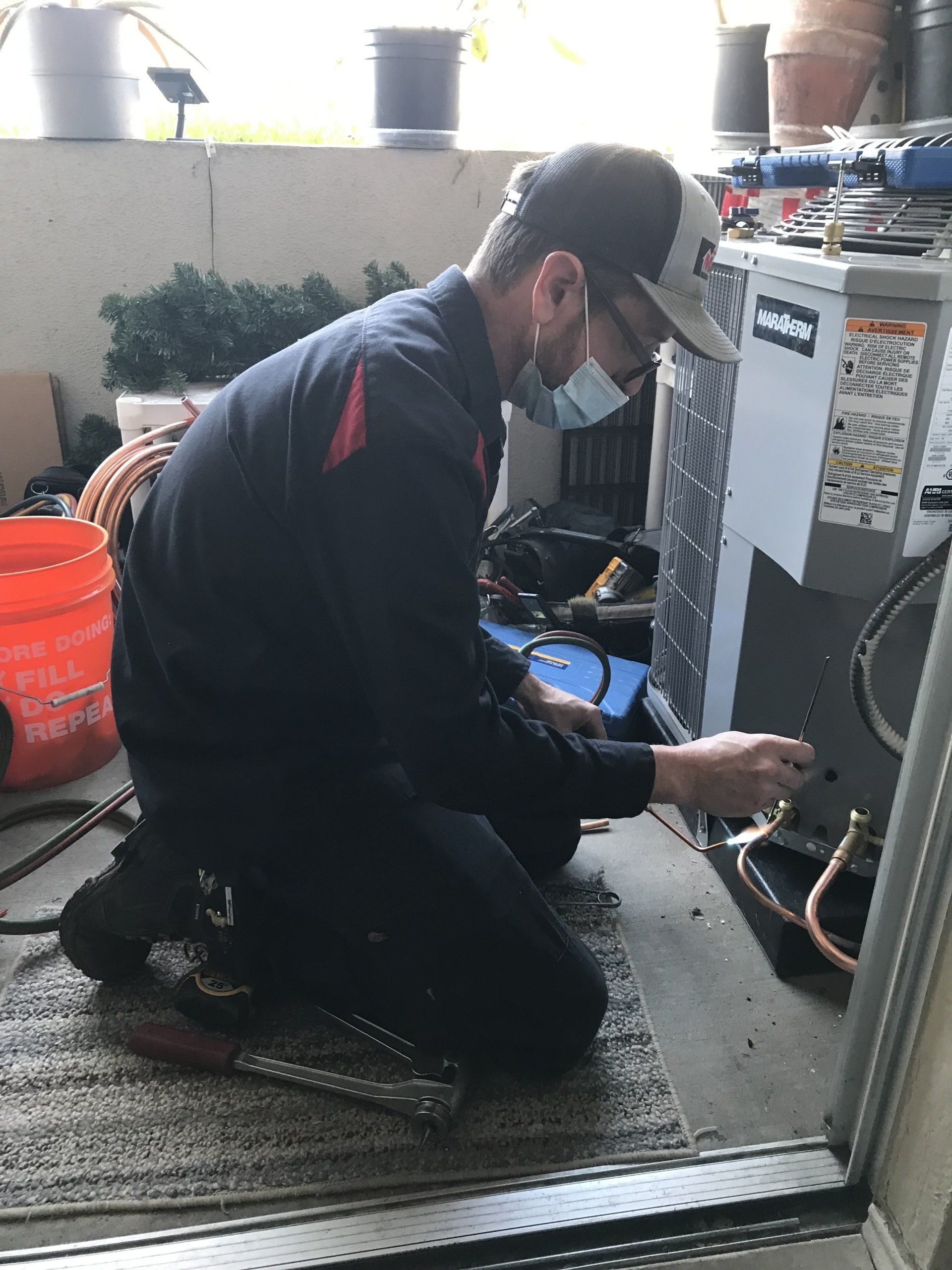 A man wearing a mask is working on an air conditioner.