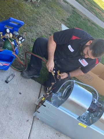 A man is sitting on the sidewalk working on an air conditioner.
