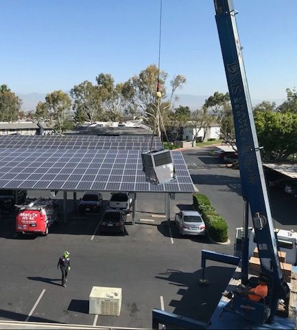A crane is lifting a box over a parking lot with solar panels.