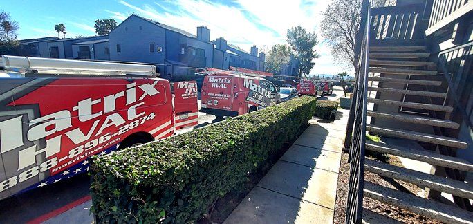 A row of red vans parked on the side of the road next to a hedge.
