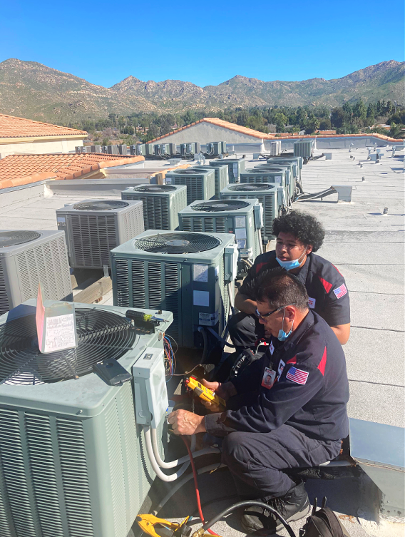 Two men are working on an air conditioner on the roof of a building.