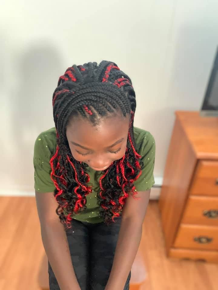 A little girl with braids in her hair is sitting on a wooden floor.