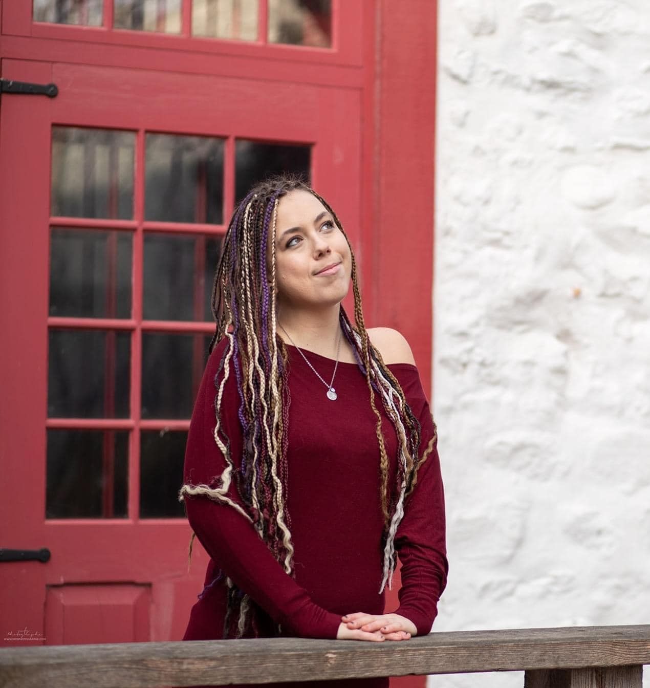 A woman with dreadlocks is standing in front of a red door.