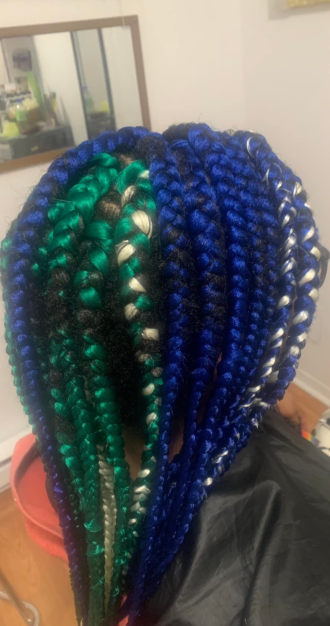 A woman with blue and green braids is sitting in front of a mirror.