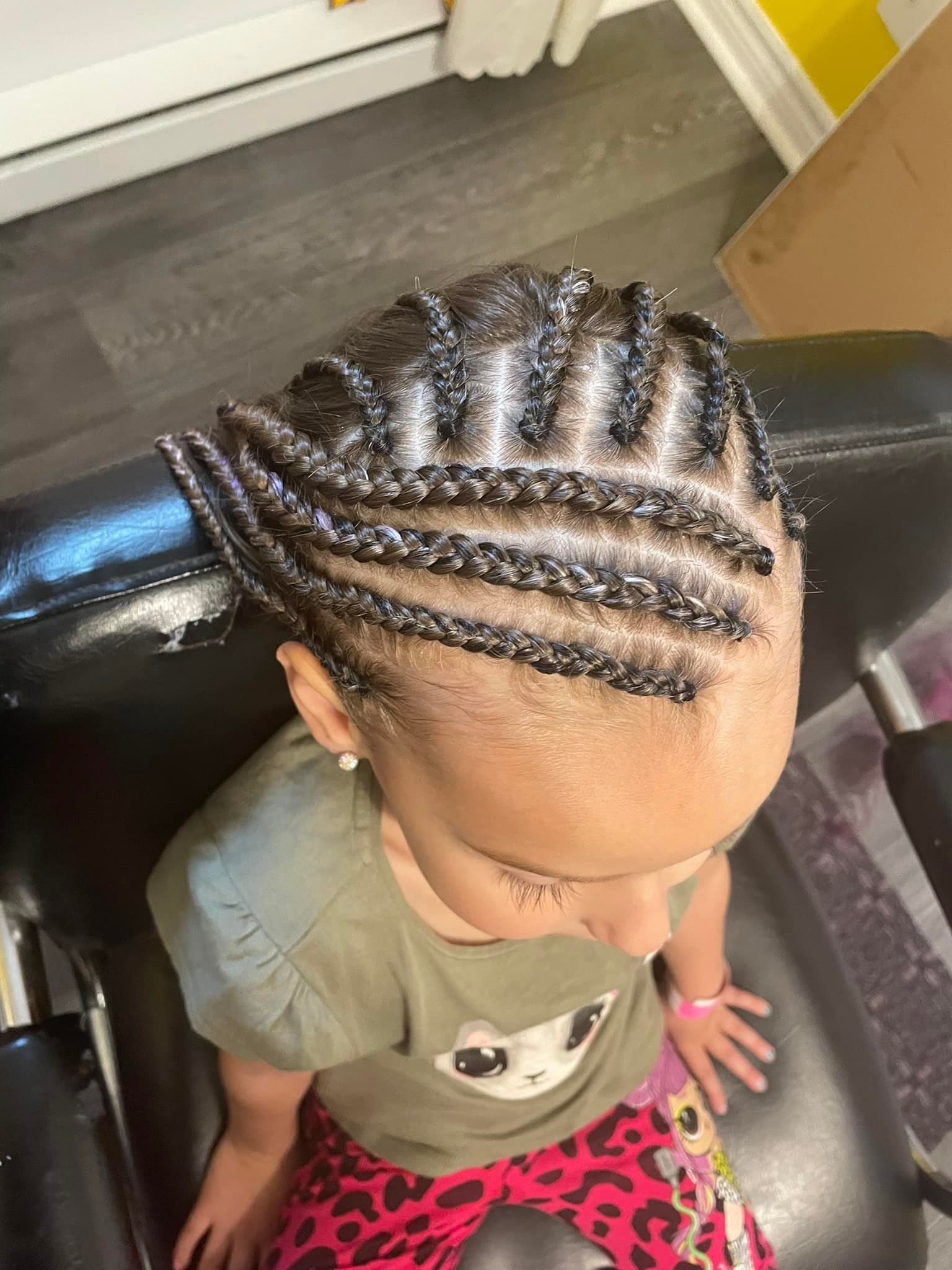 A little girl is sitting in a chair with braids in her hair.