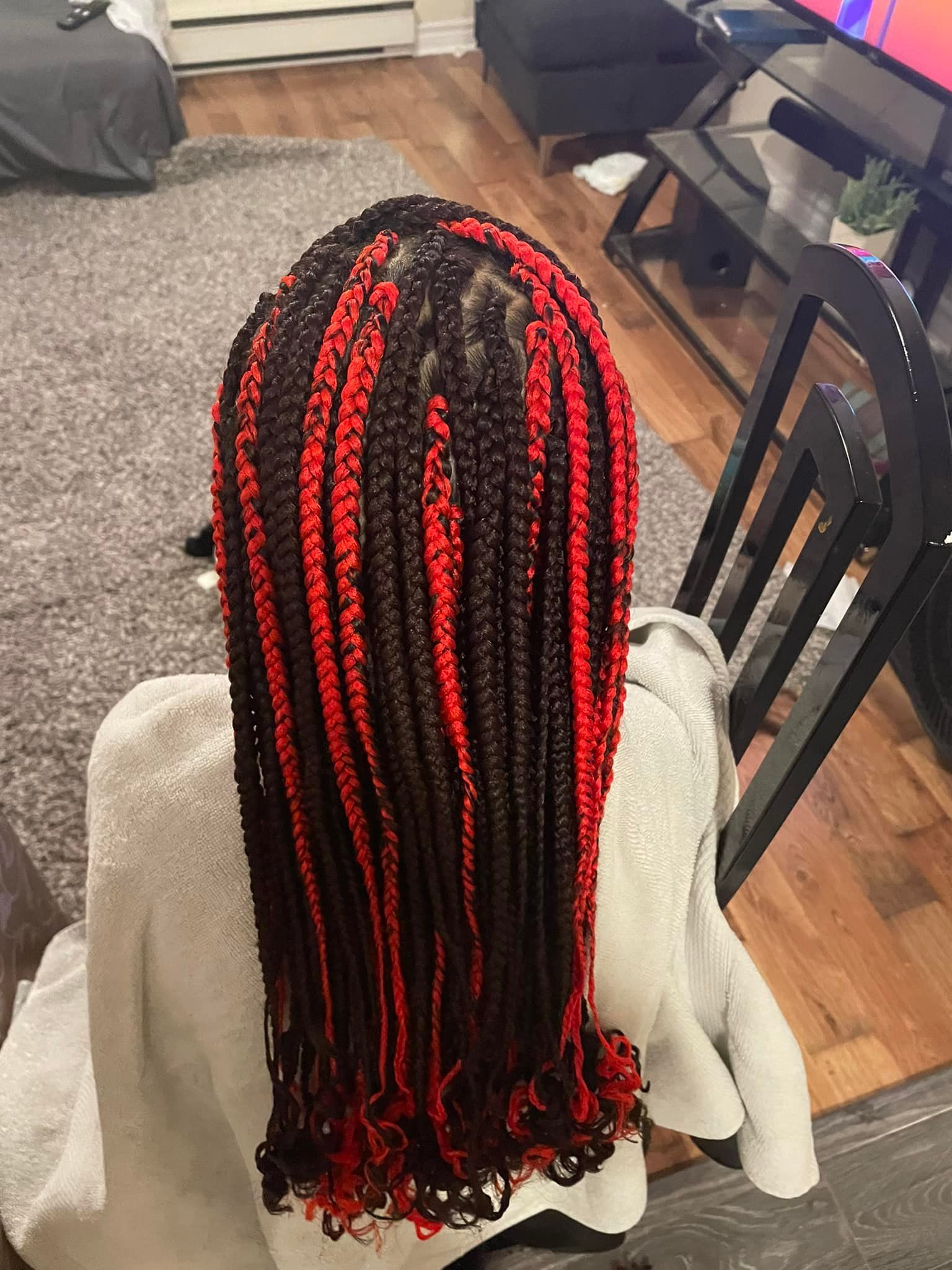 A woman with red and black braids is sitting in a chair in a living room.