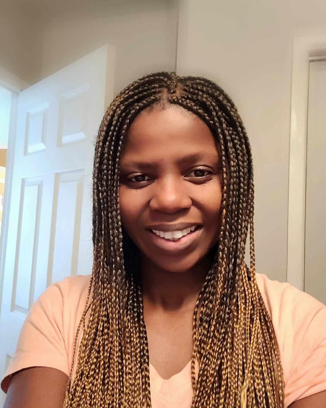 A woman with braids is smiling and wearing a pink shirt