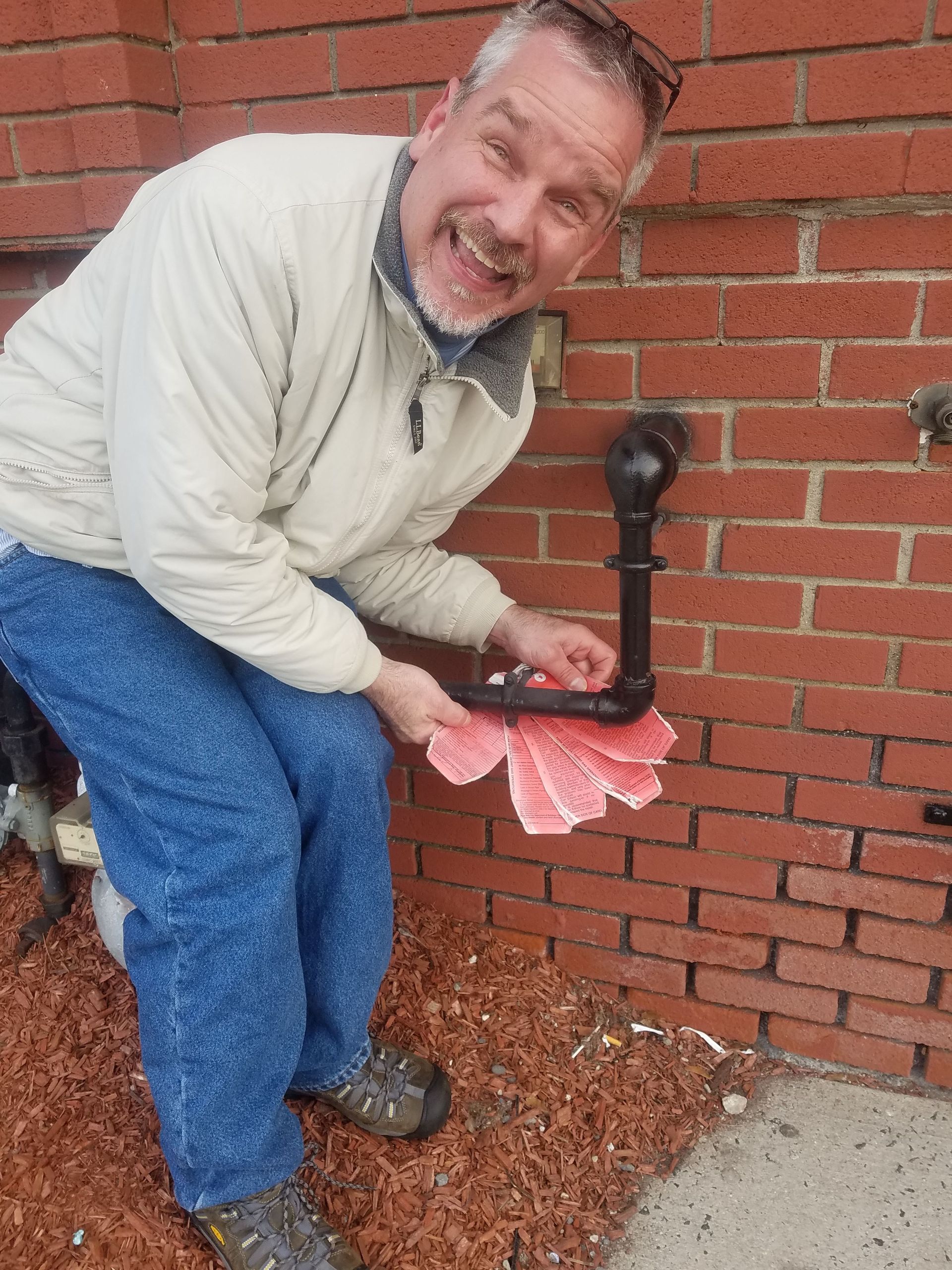 Man in jeans and a jacket smiles, holding a fanned deck of cards in front of a brick wall.