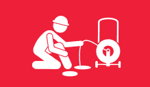 A man is kneeling down and using a hose to clean a pipe.