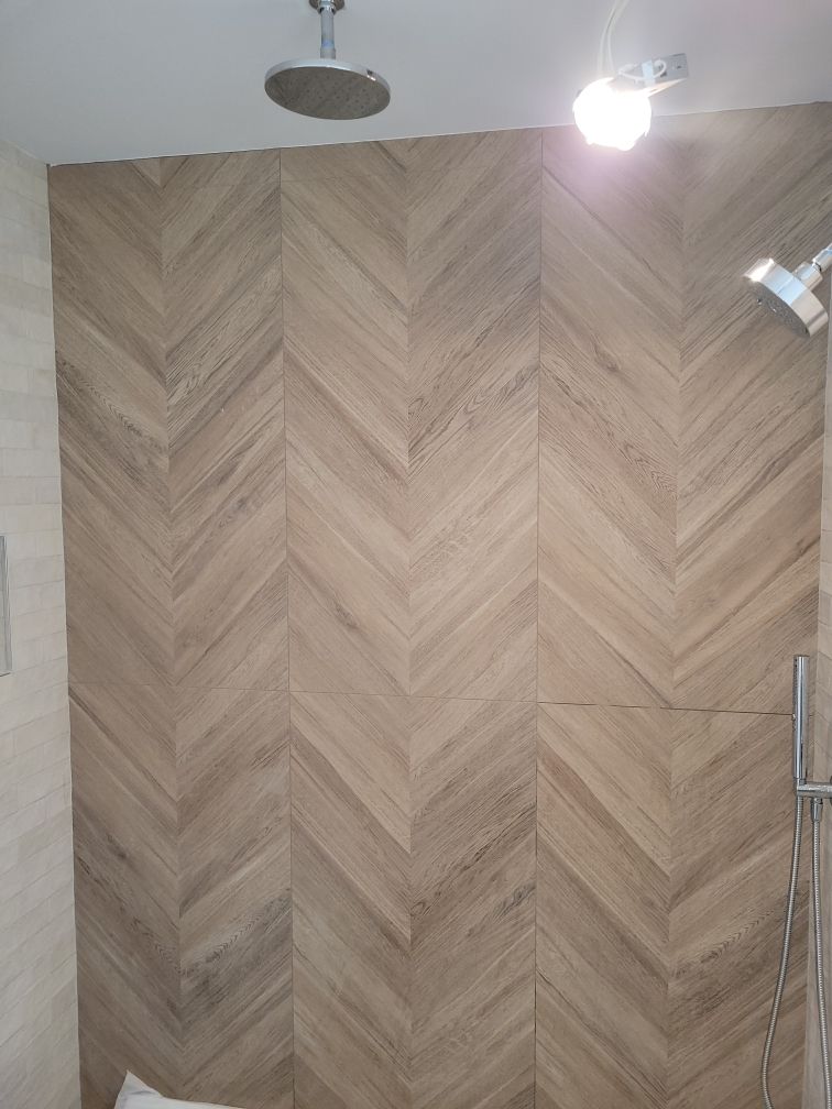 Bathroom with light brown herringbone-patterned tile wall, shower heads, and a light fixture.