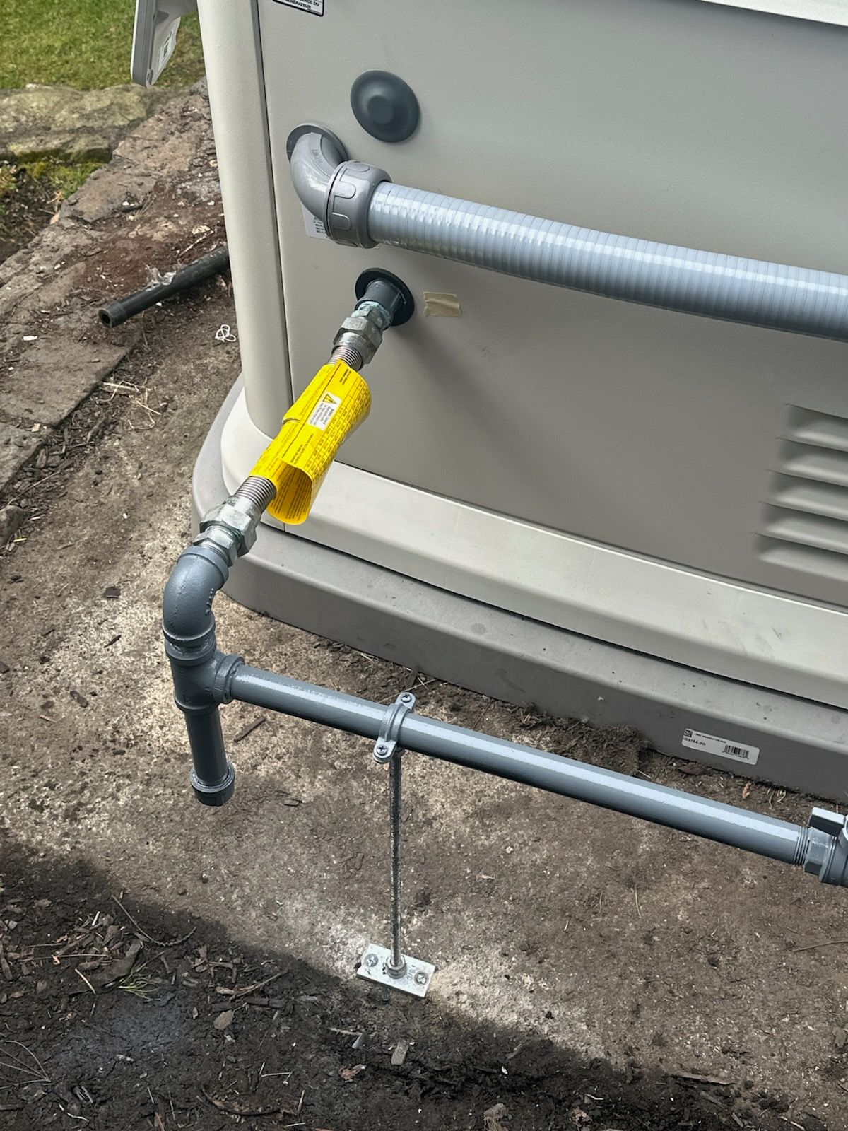 A beige generator with gray piping and a yellow gas shut-off valve installed on a concrete pad outdoors.