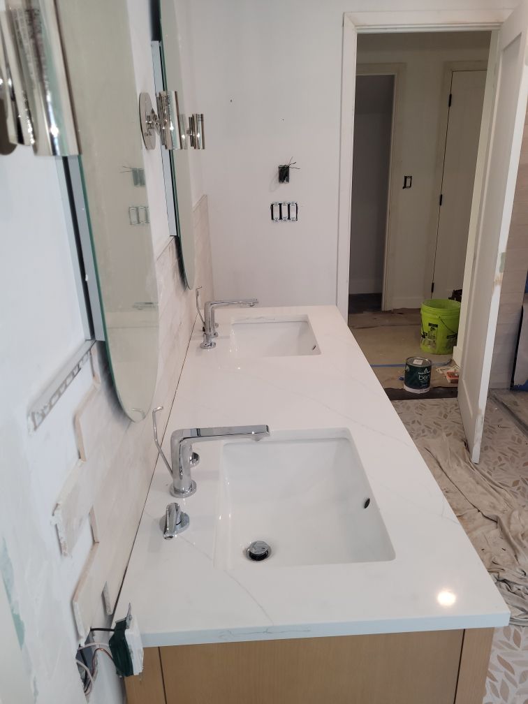 Bathroom with white walls and a vanity with two sinks and a white countertop. A mirror hangs above each sink.