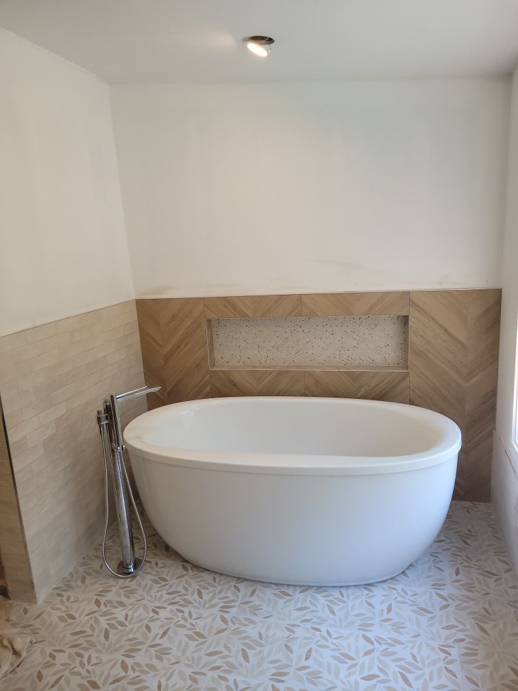 Bathroom with a white oval bathtub, light-colored tile floor with a leaf pattern, and light-colored tile on the wall.