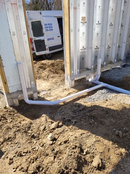A white van is parked in the dirt next to a building under construction.