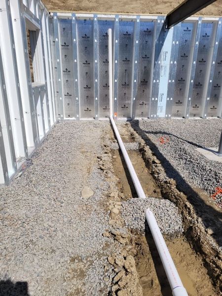 A pipe is being installed in the dirt in front of a wall.