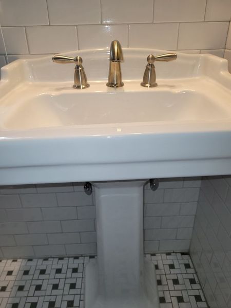 A white pedestal sink in a bathroom with white tiles