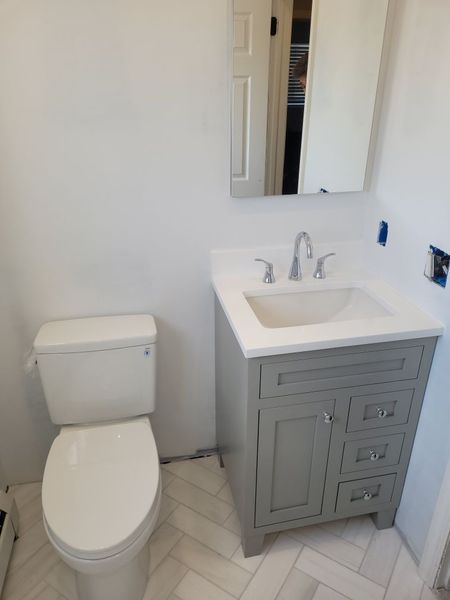 A bathroom with a toilet , sink and mirror.