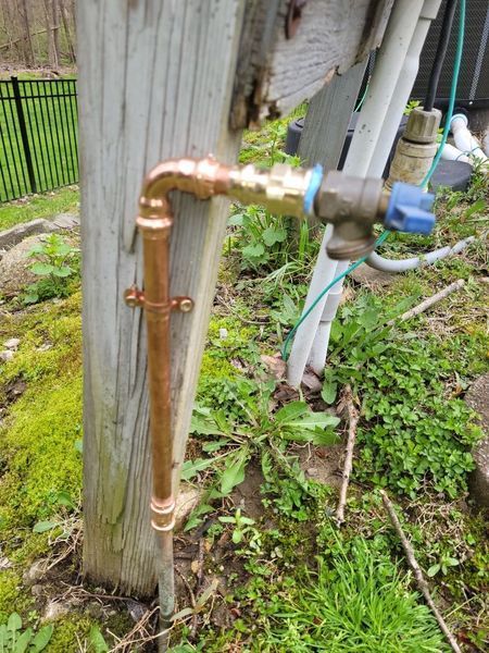 A copper pipe is attached to a wooden post in the grass.