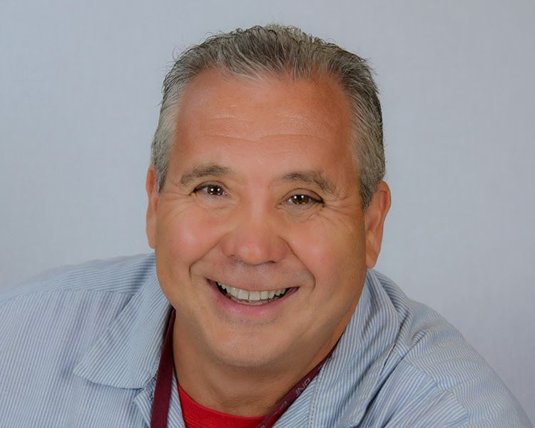 A man in a blue shirt and red shirt is smiling for the camera.